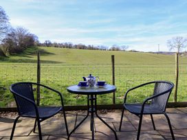 A patio with two black chairs and a table holding a teapot and cups overlooking a grassy field at The Stables in Tafarn-Y-Gelyn