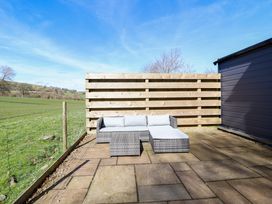 An outdoor patio with a gray wicker sectional sofa and a small table on tiled flooring next to a wooden fence and green field at The Stables in Tafarn-Y-Gelyn