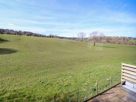 A grassy field with scattered trees and a wooden patio area at The Stables in Tafarn-Y-Gelyn