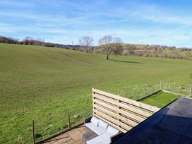 An outdoor patio with a sofa and green fields with trees in the background at The Stables in Tafarn-Y-Gelyn