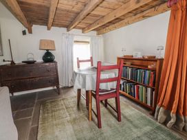 A dining area with wooden chairs a table bookshelf and a sideboard under a wooden beam ceiling at Bryn Canaid in Uwchmynydd near Aberdaron