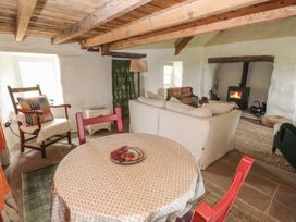 A living room with a round table covered with a cloth and a plate on top red chairs a beige sofa armchairs a wood burning stove and wooden ceiling beams at Bryn Canaid in Uwchmynydd near Aberdaron