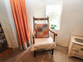 A wooden chair with a patterned cushion and a white cover next to an orange curtain and a window with a green telephone on the sill at Bryn Canaid in Uwchmynydd near Aberdaron