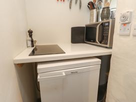 A small kitchen corner with a microwave on a counter a pepper grinder and a cooktop above a Miele fridge at Bryn Canaid in Uwchmynydd near Aberdaron