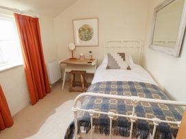 A bedroom with a single metal bed a wooden desk and stool and orange curtains at Bryn Canaid in Uwchmynydd near Aberdaron