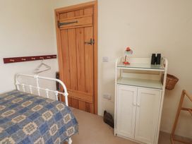 A bedroom with a wooden door white metal bed frame blue patterned blanket coat rack white cabinet with lamp and binoculars at Bryn Canaid in Uwchmynydd near Aberdaron