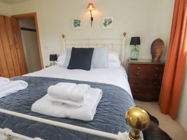 A bedroom with a bed with pillows and folded towels on a blanket a bedside table with a lamp and vase and orange curtains at Bryn Canaid in Uwchmynydd near Aberdaron