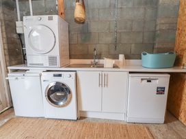 A utility room with washing machine, dryer, dishwasher, sink, and storage cabinets at Bryn Canaid in Uwchmynydd near Aberdaron