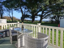 An outdoor deck with a glass table and two wicker chairs overlooking trees and a grassy field at Bay View Hillway near Bembridge