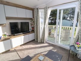 A living room with a television on a wooden cabinet and sliding glass doors leading to a balcony at Bay View in Hillway near Bembridge