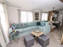 A living room with a light blue sectional sofa and patterned cushions a small black side table with flowers and a wooden coffee table with two gray ottomans at Bay View Hillway near Bembridge