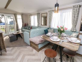 A dining area with a wood table set for four and a light blue corner sofa in a living room with sliding glass doors and curtains at Bay View in Hillway near Bembridge