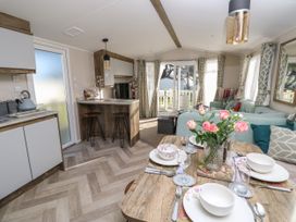 An open kitchen dining and living area with a wooden dining table set with dishes and flowers and a seating area with a sofa and large windows at Bay View in Hillway near Bembridge