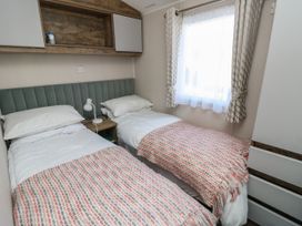 A bedroom with two single beds a bedside table with a lamp a window with curtains and overhead cabinets at Bay View Hillway near Bembridge