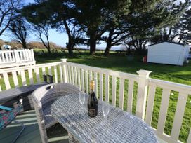 A patio with a wicker table and chair a bottle of wine and two glasses overlooking a grassy area with trees and a white shed at Bay View in Hillway near Bembridge