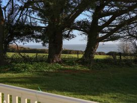 A view of the ocean through trees with grass and a wooden fence in the foreground at Bay View in Hillway near Bembridge