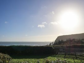 A seaside view with a grassy garden and hedge in the foreground a wooden fence to the right and a cliff under a bright sun at Bay View Hillway near Bembridge