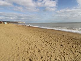 A sandy beach with a few people walking near the shoreline and cliffs in the distance at Bay View in Hillway near Bembridge