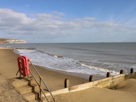A sandy beach with waves coming in and a lifebuoy on a railing near wooden groynes at Bay View Hillway near Bembridge