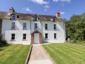 A white two-story house with a brick entrance and a tiled roof with dormer windows and a lawn in front at Glanduad Fawr in Newport Pembrokeshire