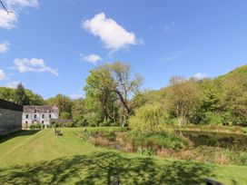 A garden with a pond trees benches and a white house in the background at Glanduad Fawr Newport Pembrokeshire