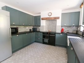 A kitchen with green cabinets a black oven a clock on the wall and a stainless steel refrigerator at Glanduad Fawr Newport Pembrokeshire