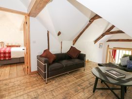 A sitting area with black leather sofas brown cushions and a glass coffee table next to a bedroom with a red blanket at Glanduad Fawr in Newport Pembrokeshire