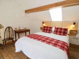 A bedroom with a bed featuring red patterned cushions and runner a wooden chair and a small wooden desk at Glanduad Fawr in Newport Pembrokeshire
