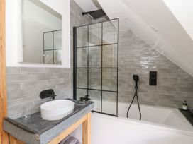 A bathroom with a bathtub under a slanted ceiling a shower screen a round sink on a counter and a mirror at Glanduad Fawr in Newport Pembrokeshire