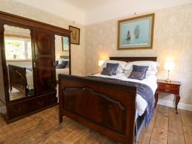 A bedroom with a wooden bed and wardrobe a nightstand with a lamp and paintings on the wall at Glanduad Fawr in Newport Pembrokeshire