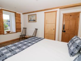 A bedroom with a bed covered in patterned bedding, two wooden chairs, a small round table, wooden window shutters, and two doors at Glanduad Fawr in Newport Pembrokeshire