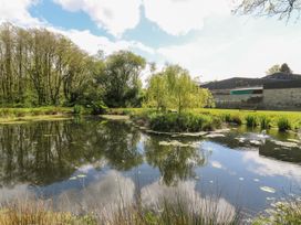 A pond surrounded by trees and grass with a small island and a bench at Glanduad Fawr in Newport Pembrokeshire
