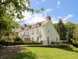 A white two-story house with chimneys and a fenced patio area surrounded by trees and grass at Glanduad Fawr in Newport Pembrokeshire