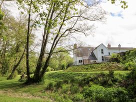 A white house with a sloped roof surrounded by trees and greenery at Glanduad Fawr in Newport Pembrokeshire