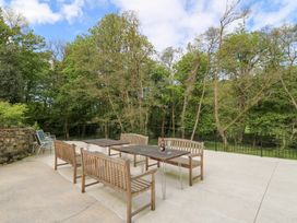 An outdoor patio with wooden benches and tables surrounded by trees at Glanduad Fawr in Newport Pembrokeshire