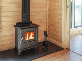 A wood burning stove with fire inside on a black hearth in a wooden room at Primrose in Higher Wambrook near Chard