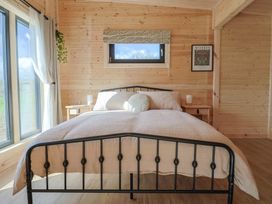 A bedroom with a bed a window with curtains and wooden walls at Primrose in Higher Wambrook near Chard