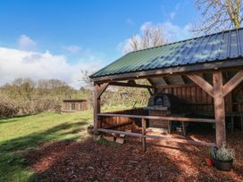 An outdoor covered wooden shelter with a brick oven and wood chips on the ground at Primrose in Higher Wambrook near Chard