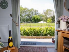 A room with an open door showing a garden with trees and an umbrella with curtains on each side and a bottle of prosecco on a table at Yes Deer in Ashbourne