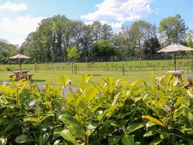 An outdoor area with picnic tables and umbrellas behind a hedge with trees and grass in the background at Yes Deer in Ashbourne