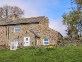 A stone house with a white door and windows surrounded by a grassy yard with yellow flowers and trees at Swinhope View in Hexham