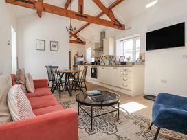 A living area with a red sofa, round glass coffee table, dining table with black chairs, kitchen cabinets, and a wall-mounted TV at Guillemot in Flamborough
