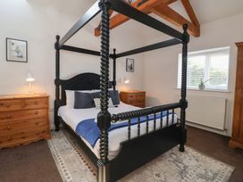A bedroom with a black four-poster bed two wooden dressers lamps a window and a rug at Guillemot in Flamborough