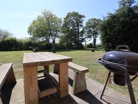 A wooden picnic table with benches on a patio and a charcoal grill in a grassy garden area with trees in the background at Guillemot in Flamborough