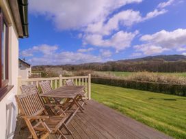 A deck with a table and chairs overlooking a field at Country Cottage in Brecon