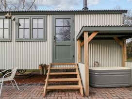 An exterior view of a corrugated metal building with green framed windows and door wooden steps leading to the door a covered outdoor grey bathtub and a white metal chair on a paved patio at Evendine Hut @ Evendine Cottage in Colwall Herefordshire