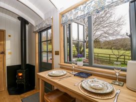 A dining area with a wooden table set for two beside a window showing an outdoor view and a black wood-burning stove in the corner at Evendine Hut @ Evendine Cottage Colwall Herefordshire
