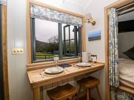A small dining area with two stools and table set for two by a window with floral curtains at Evendine Hut @ Evendine Cottage in Colwall Herefordshire