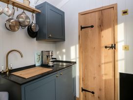 A kitchen corner with blue cabinets a wooden door hanging pots a brass faucet and a coffee machine at Evendine Hut @ Evendine Cottage Colwall Herefordshire