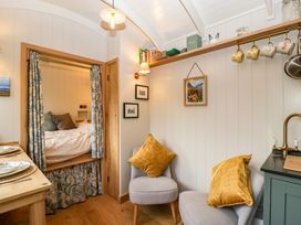 A small room with two chairs with yellow cushions a wooden table set with plates a built-in bed with curtains and shelves with mugs and books at Evendine Hut @ Evendine Cottage Colwall Herefordshire